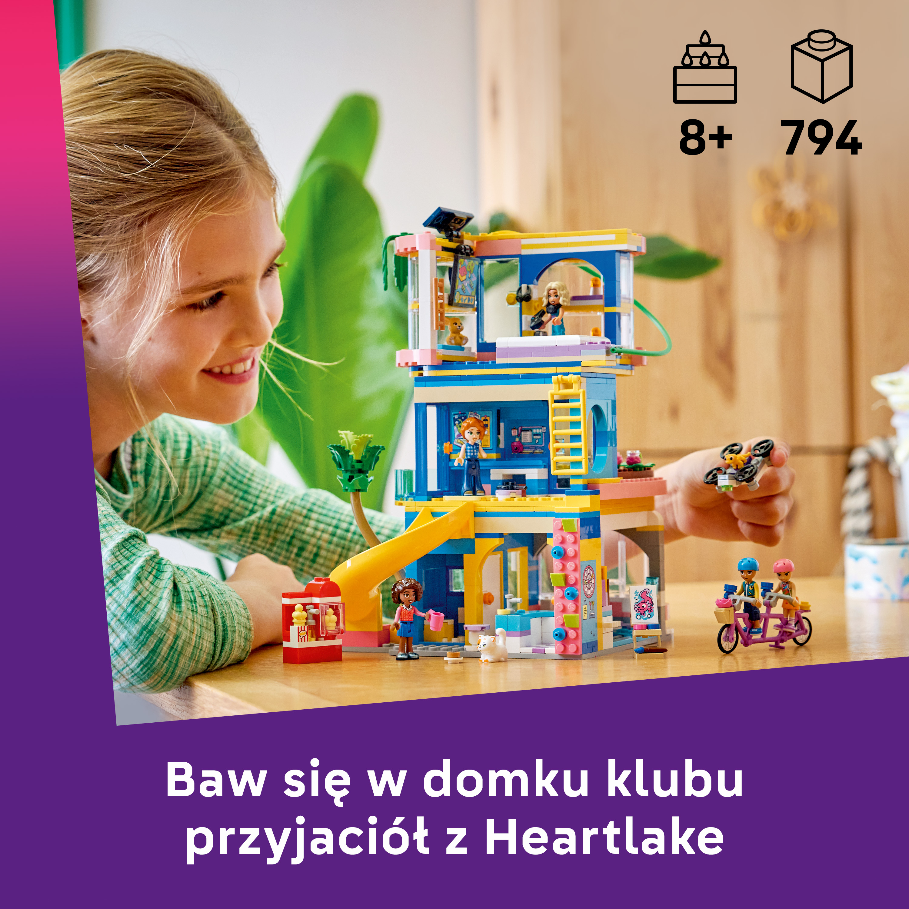 Dziewczynka uśmiecha się, patrząc na kolorowy dom klubowy Lego z postaciami.