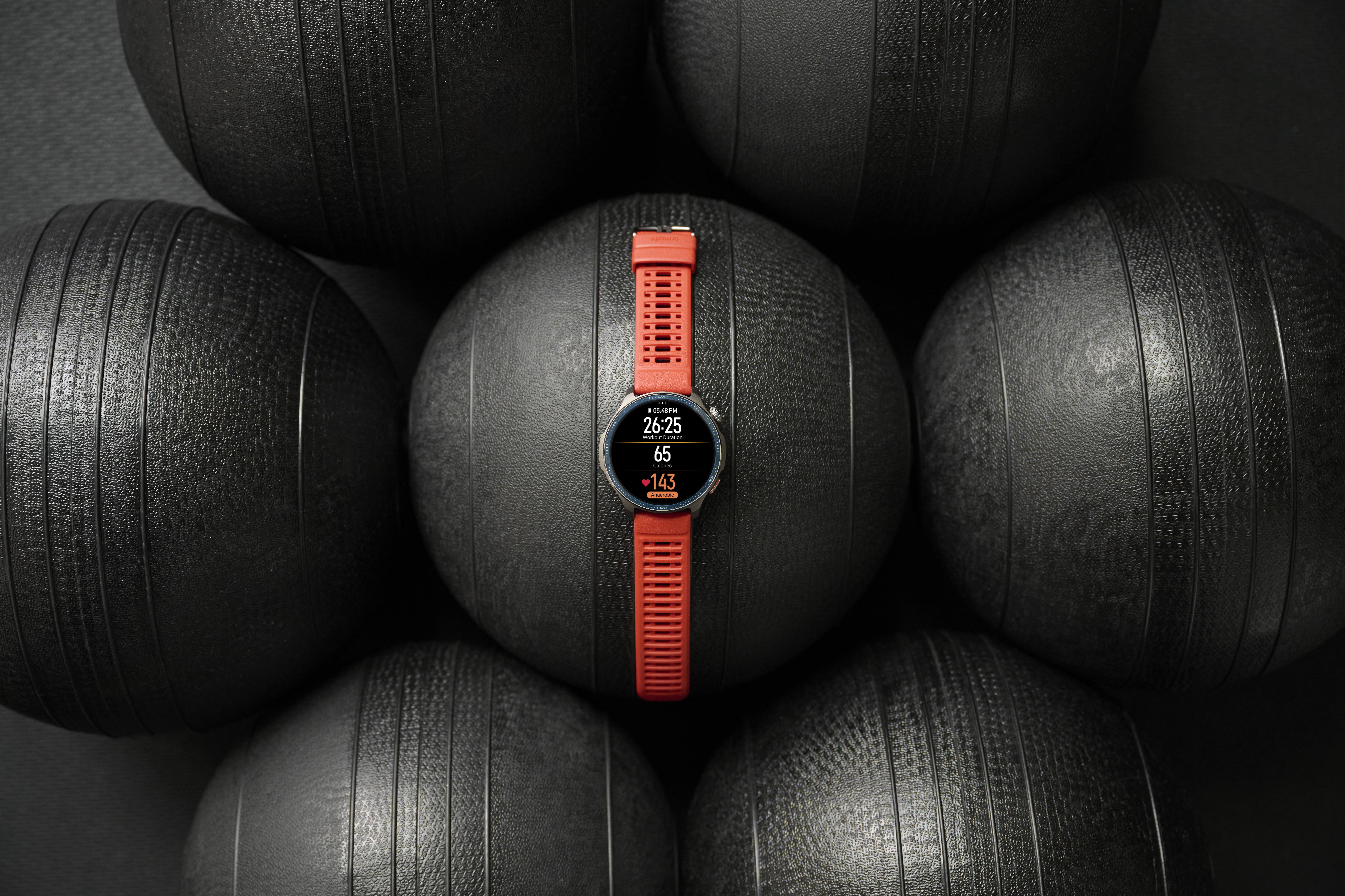 Czerwony smartwatch z danymi dotyczącymi kondycji leży na czarnych piłkach lekarskich.