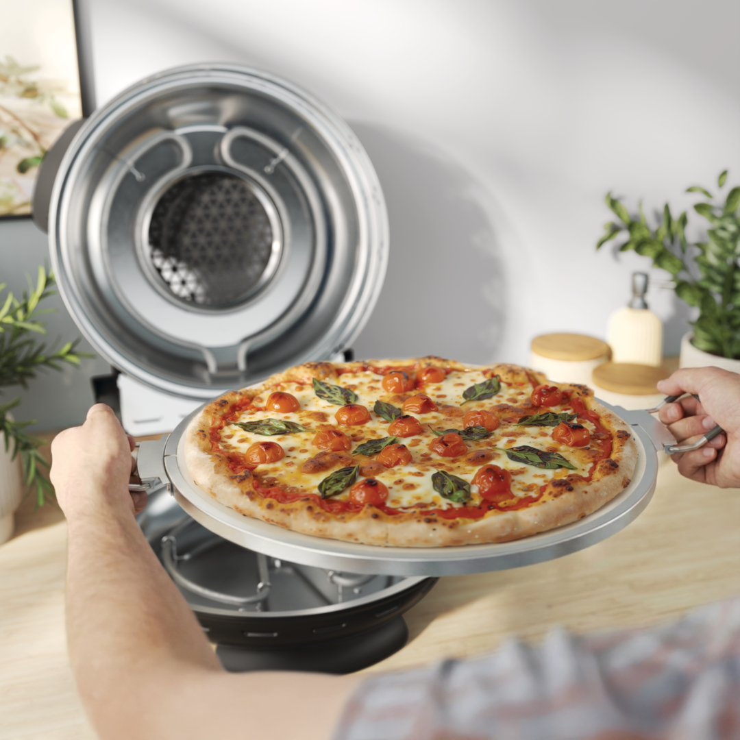 Eine Person schiebt eine Pizza mit Tomaten und Basilikum in einen Ofen.