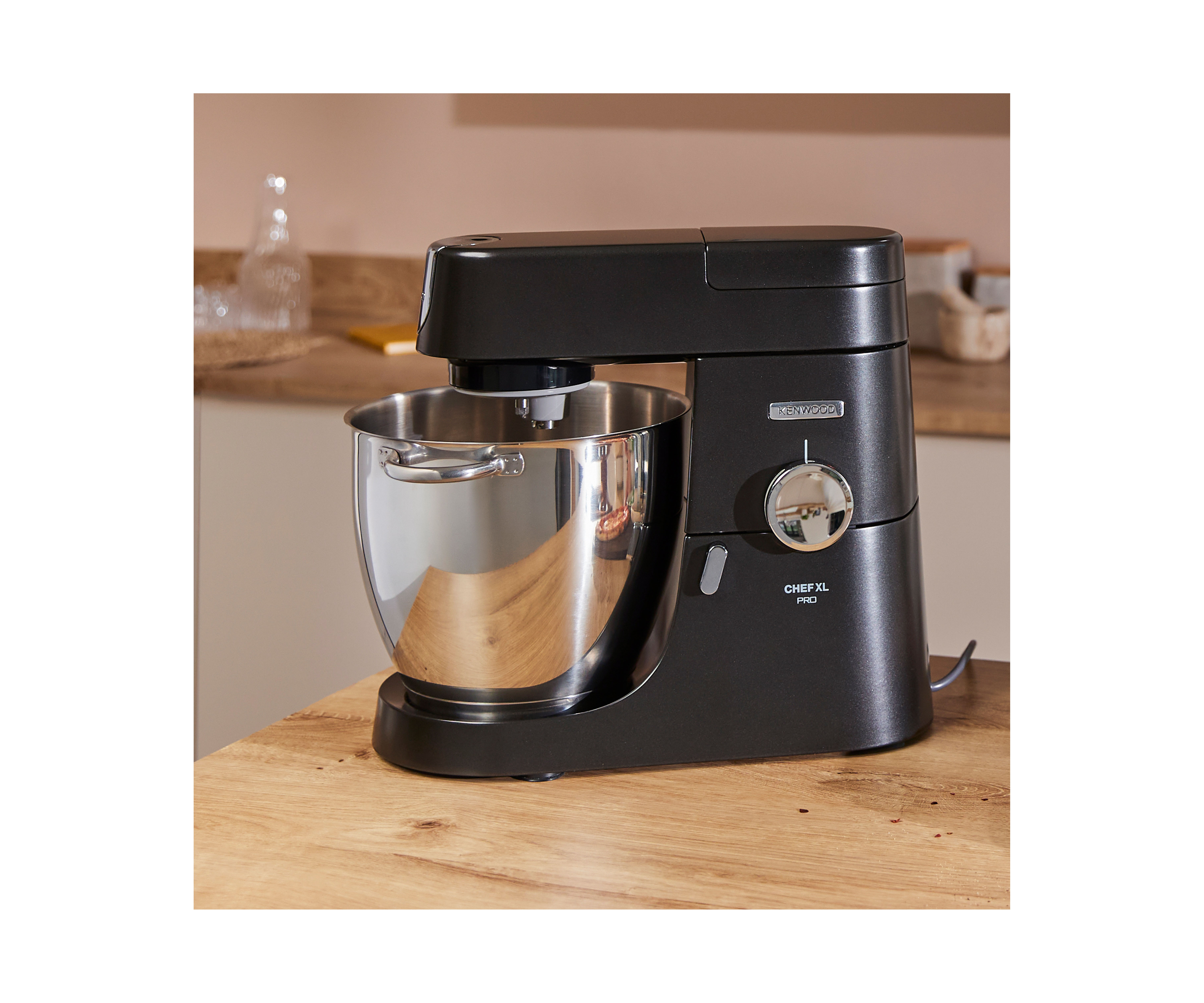 Schwarzer Kenwood Küchenmixer mit Edelstahlschüssel auf Holztisch.