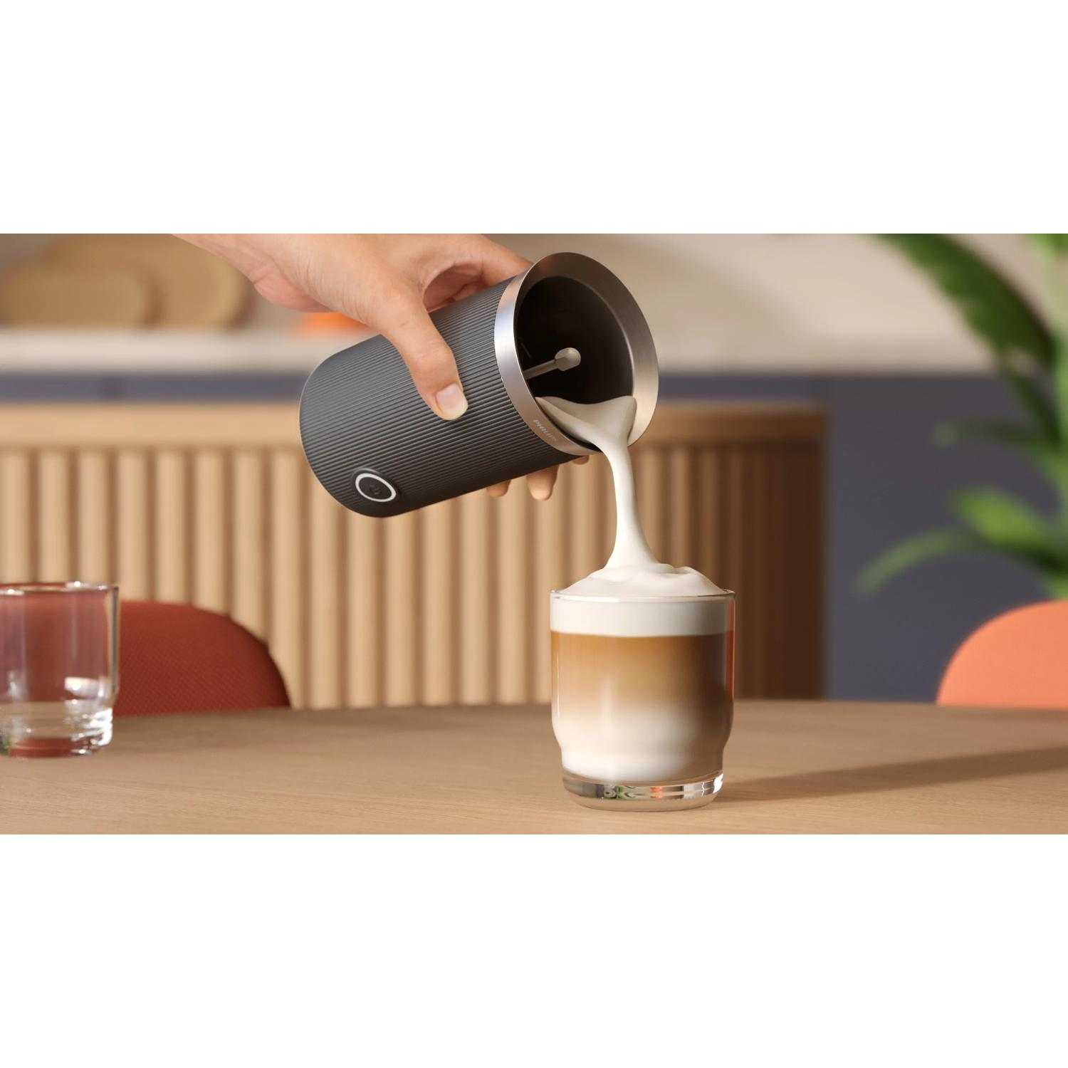 Una mano vierte espuma de leche de un recipiente oscuro en un vaso de café.