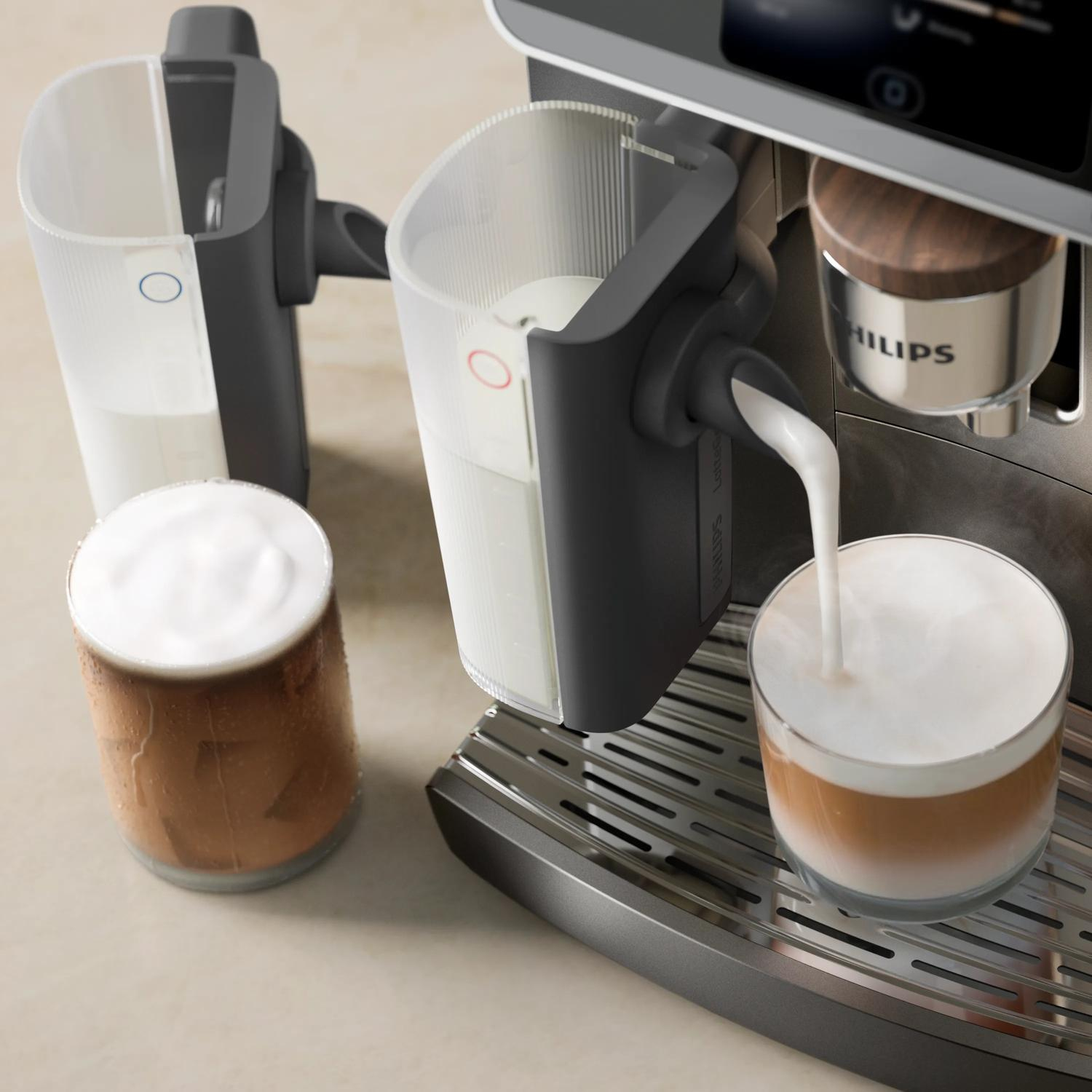 Una cafetera espumea leche en un vaso, junto a un vaso con café.