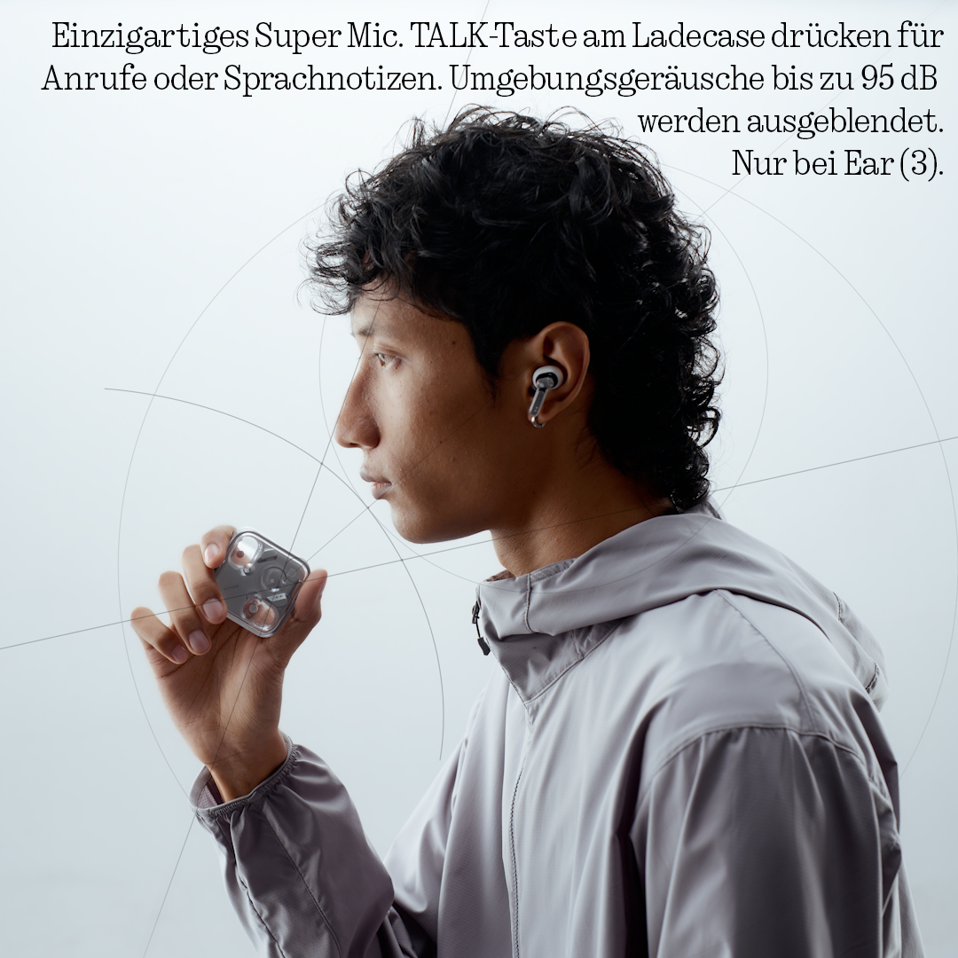 Mann mit Kopfhörern hält Ladecase. Grauer Windbreaker, weißer Hintergrund.