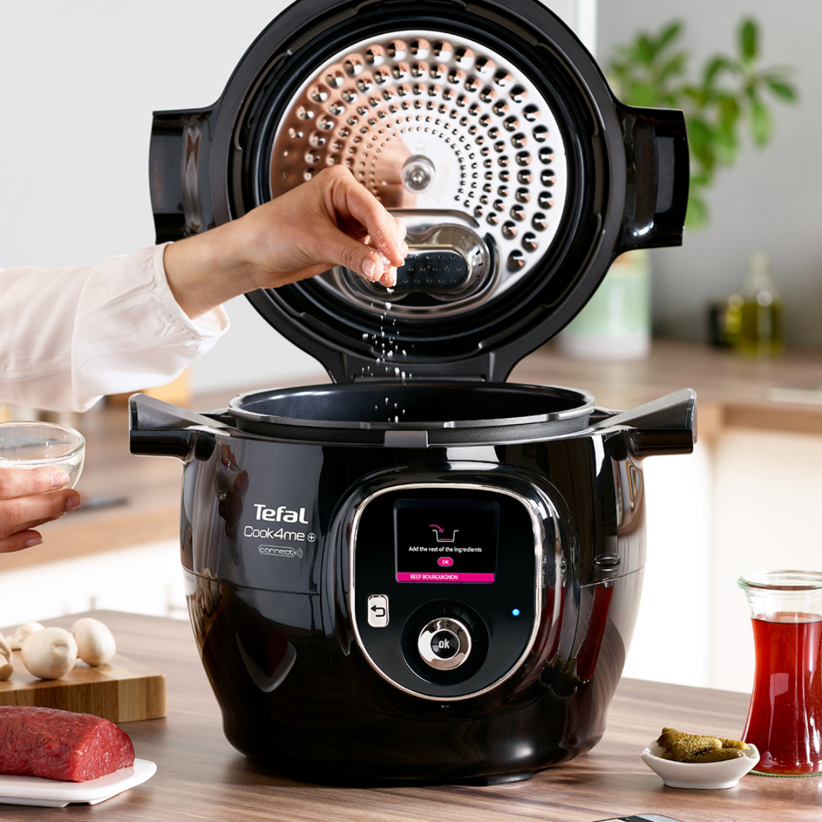 Egy kéz sót szór egy nyitott fekete Tefal Cook4Me főzőedénybe.