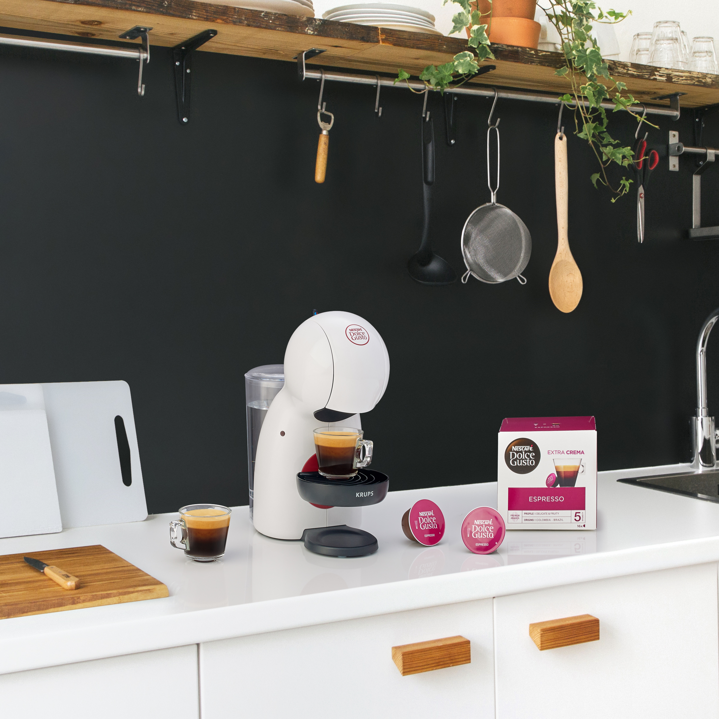 Egy fehér Nespresso kávéfőző eszpresszókapszulákkal és egy dobozzal a pulton.