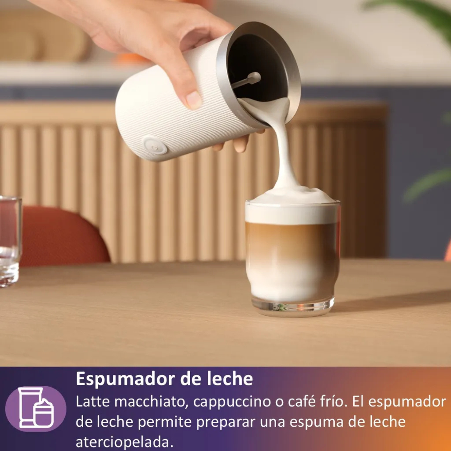 Una mano vierte leche espumada de un espumador blanco en un vaso de café.
