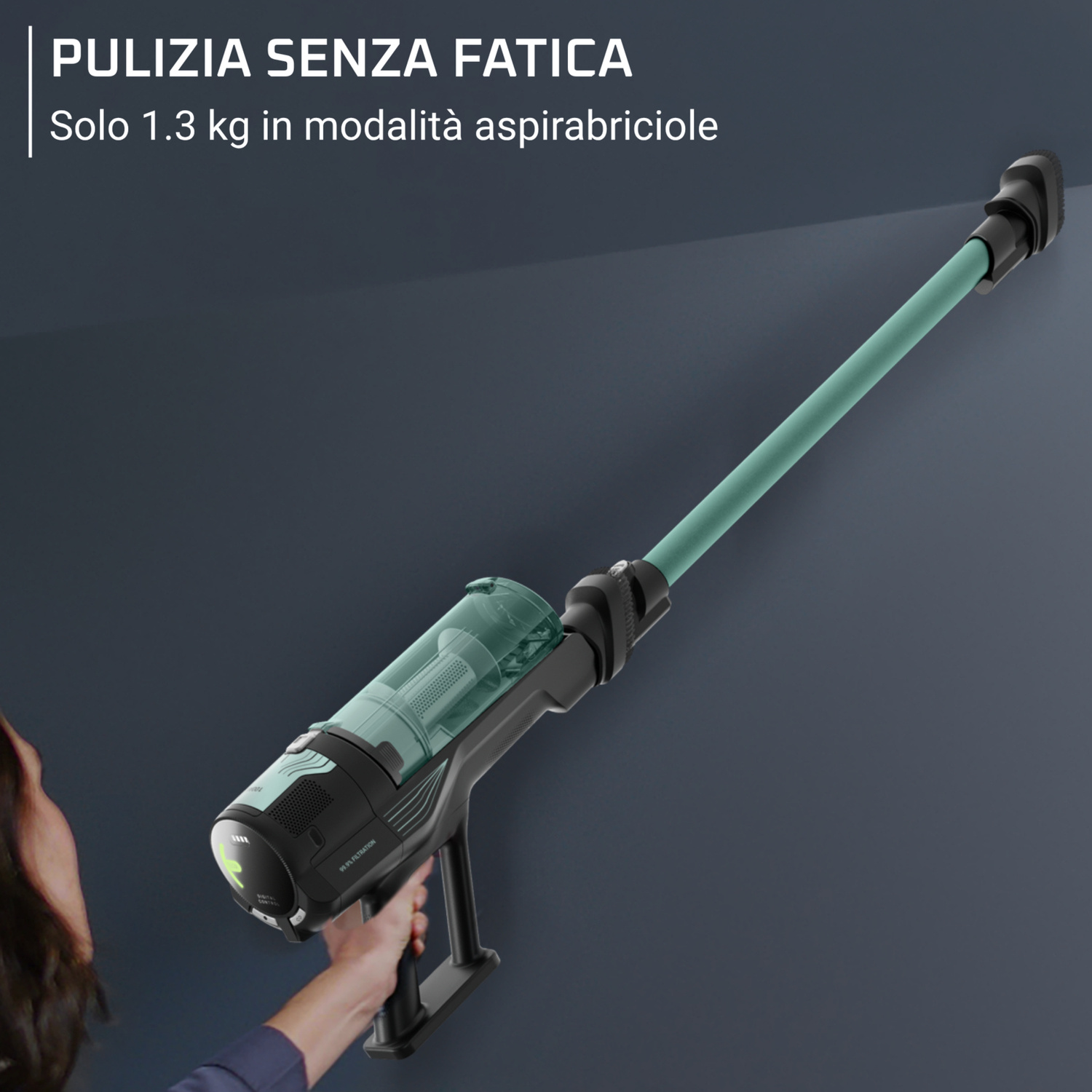 Una persona tiene un aspirapolvere senza fili leggero verde e nero contro un muro scuro.