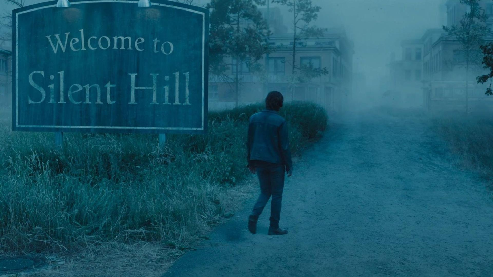 Eine Person geht auf einem Weg auf Gebäude in einer nebligen Stadt zu. Ein Schild sagt 'Willkommen in Silent Hill'.