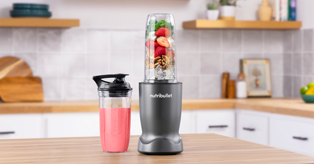 Ein grauer Nutribullet-Mixer mit Erdbeeren, Nüssen und Eis in einem Glasaufsatz.