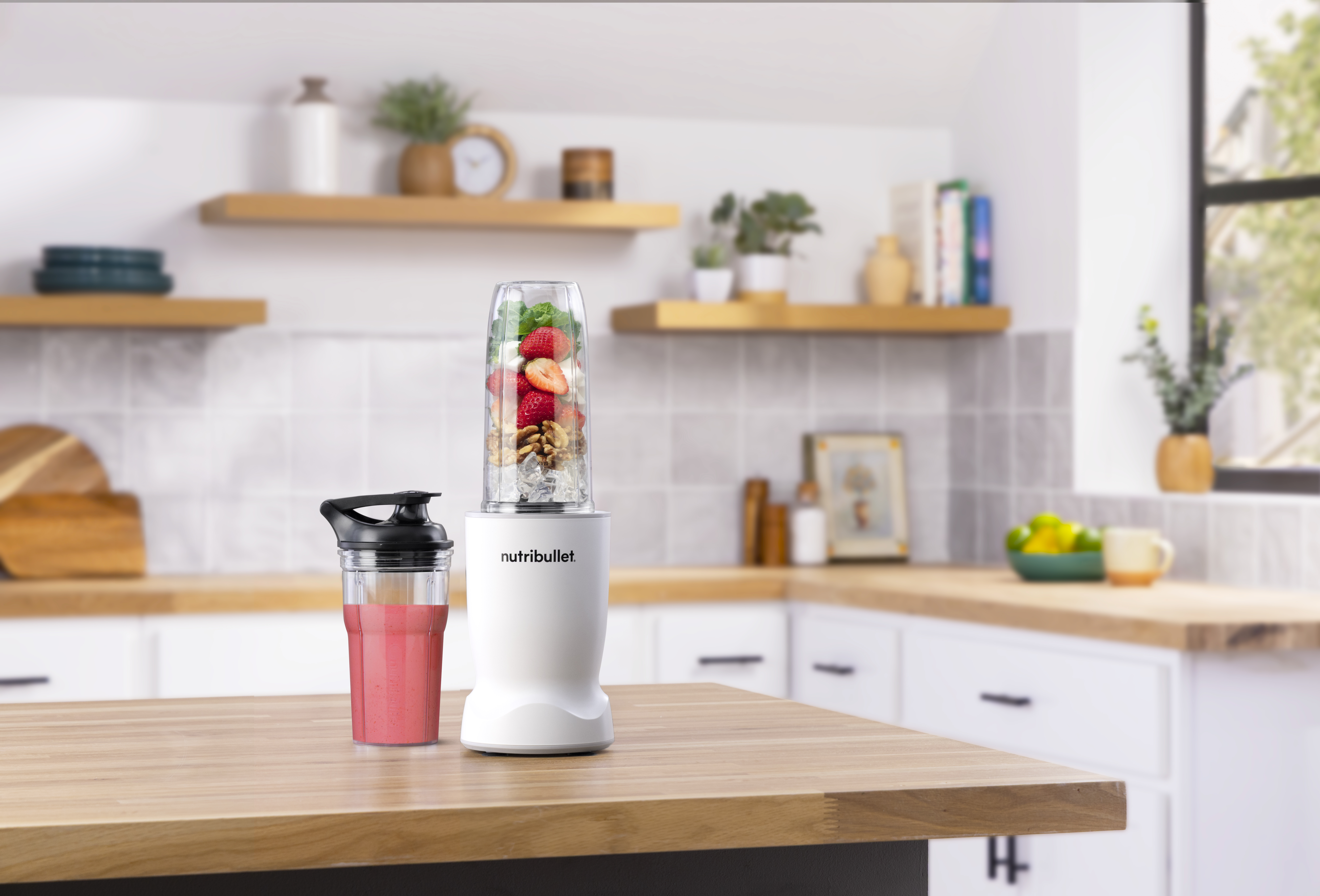 Ein weißer Nutribullet Mixer mit einem gefüllten Behälter und einem Glas Smoothie.