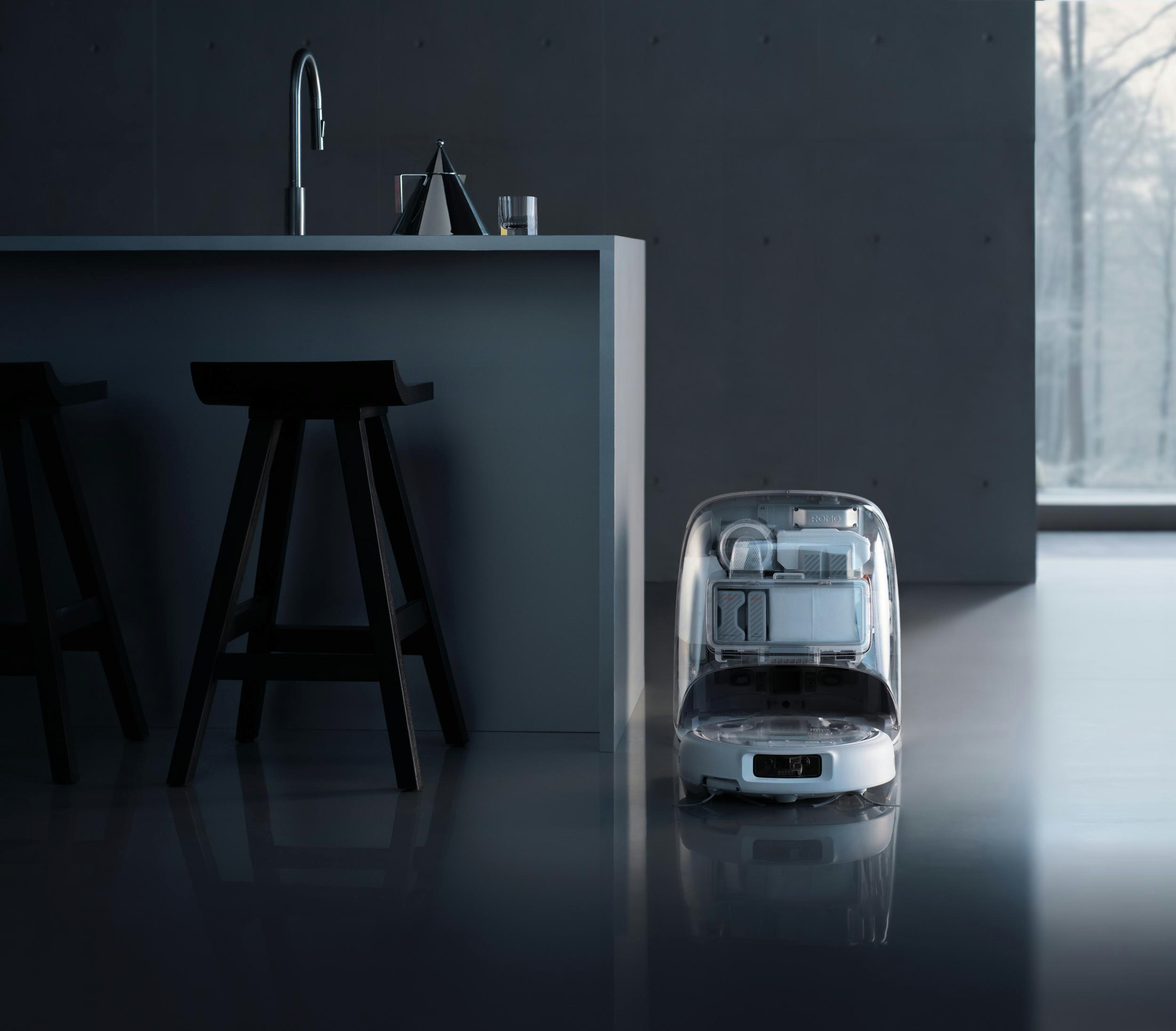 Ein transparenter Reinigungsroboter steht neben einer Kücheninsel mit Hockern.
