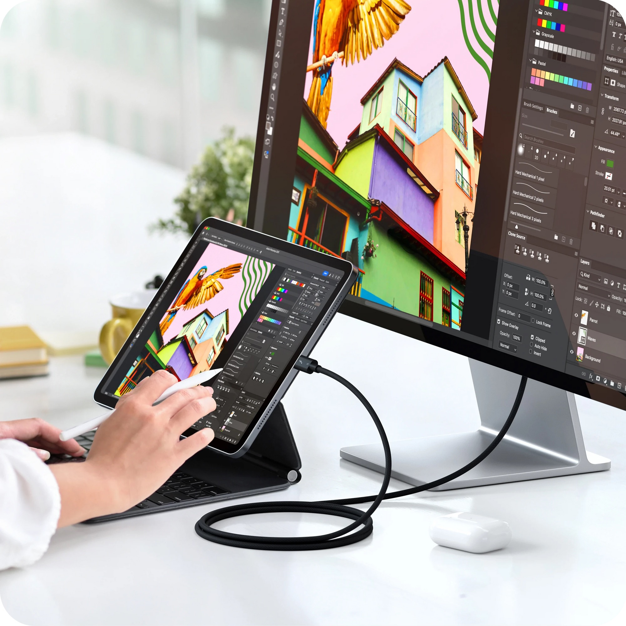 Une personne utilise une tablette connectée à un moniteur, éditant une image colorée de bâtiments et d'un perroquet.