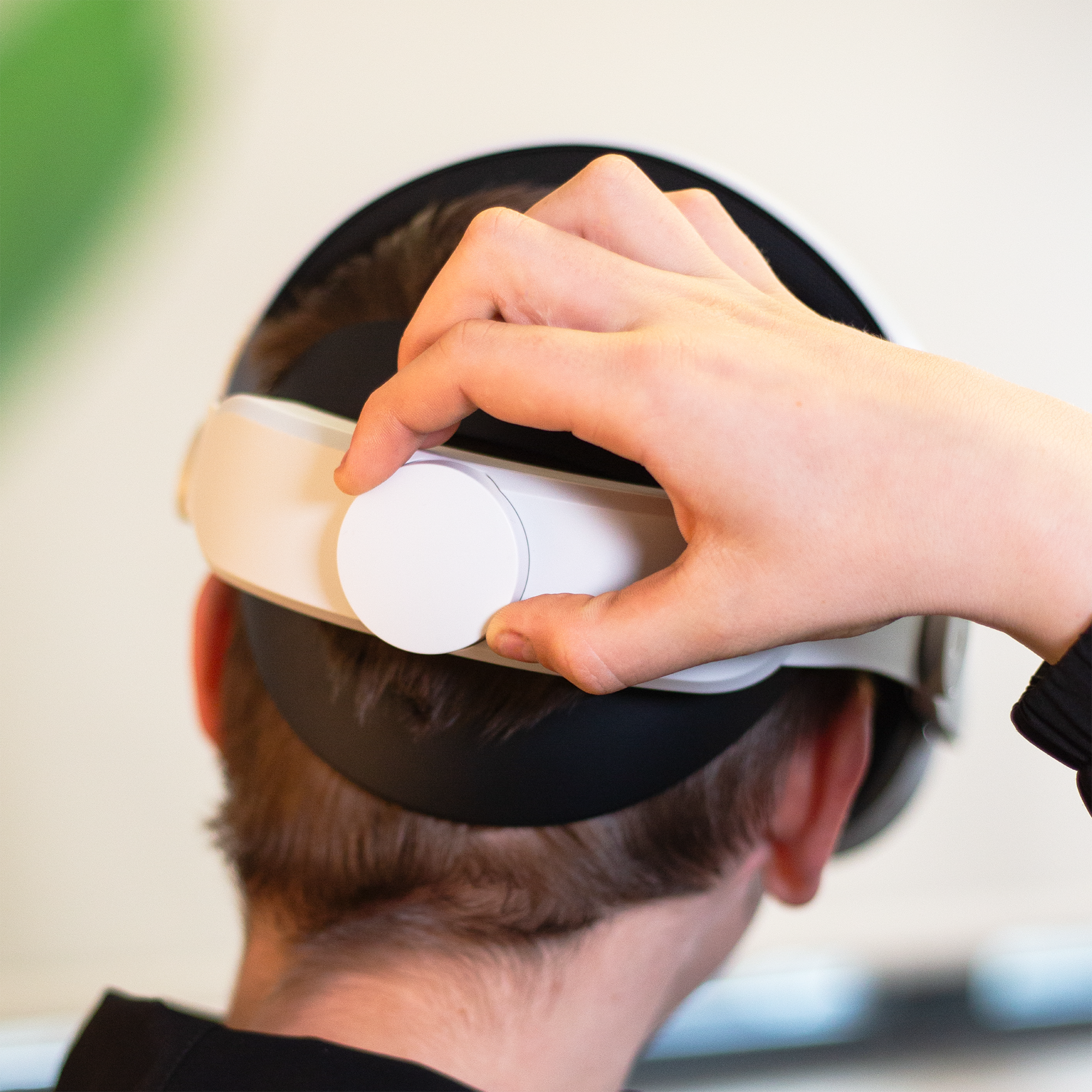Eine Hand stellt einen Regler an einem weißen VR-Headset ein.