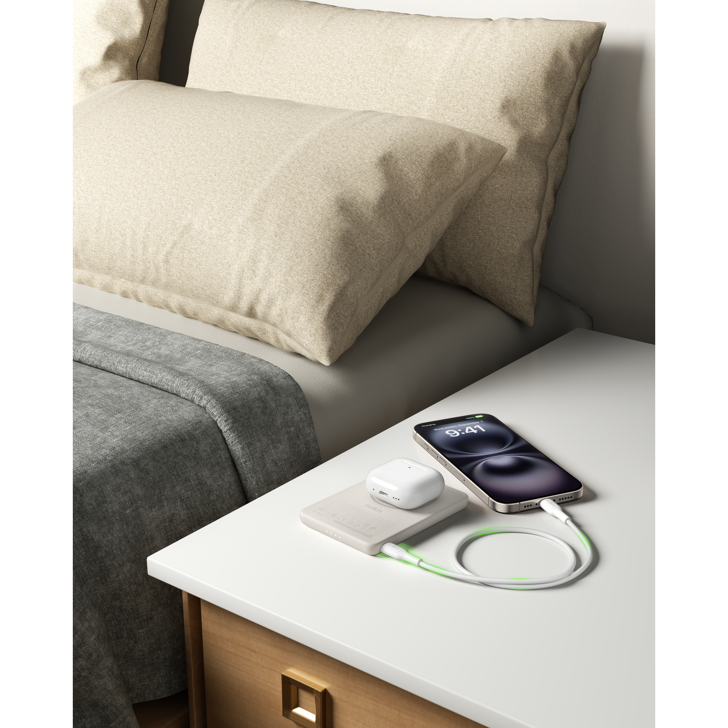 A nightstand with a smartphone, AirPods, and a power bank being charged.