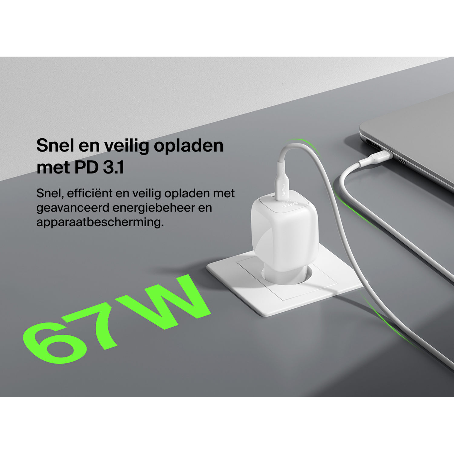 A white 67W charger plugged into an outlet, charging a laptop.