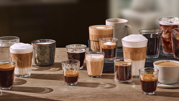 Mehrere Kaffeegläser und Tassen mit verschiedenen Kaffeesorten auf einem Holztisch.