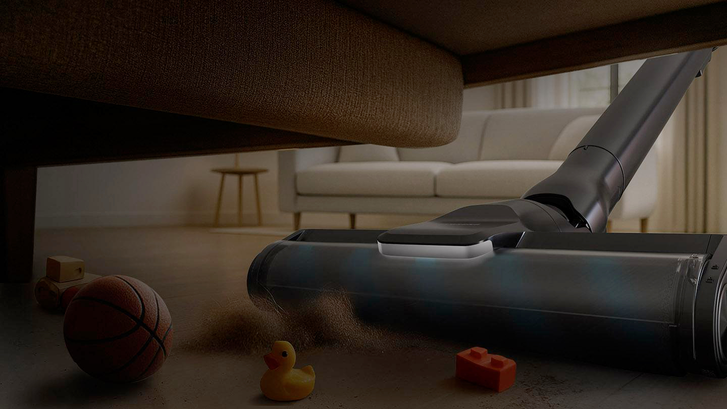 Staubsauger unter Couch sammelt Staub nahe Spielzeug: Ball, Ente, Ziegel.