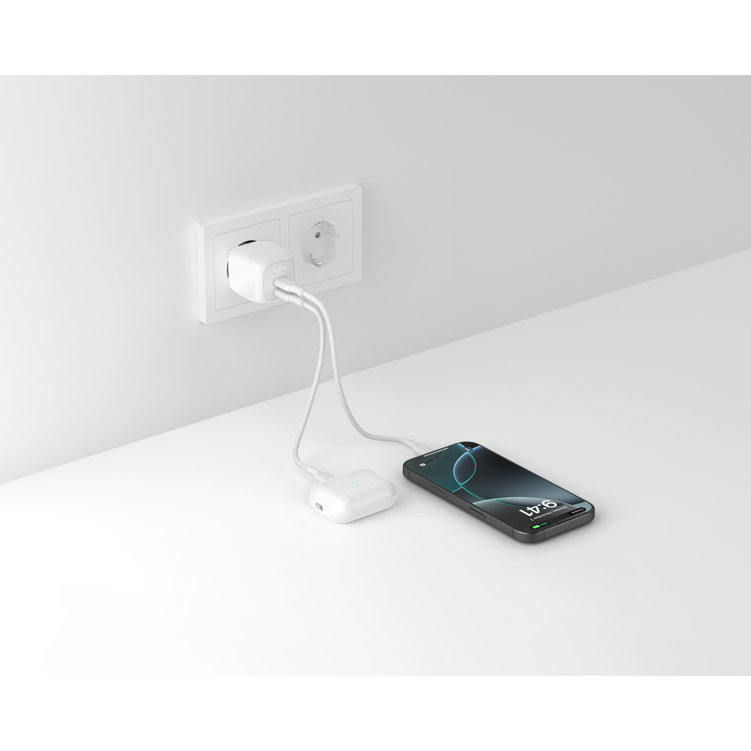 A white power adapter charges a smartphone and earbuds via white cables.