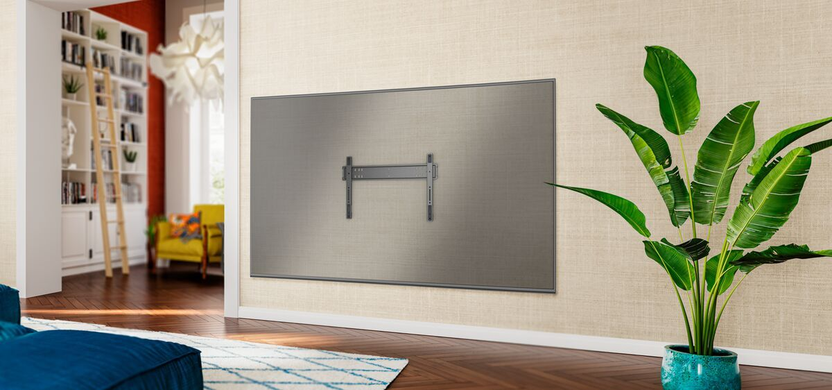 Un televisor grande y gris con soporte de pared en una pared beige. Una planta a la derecha.