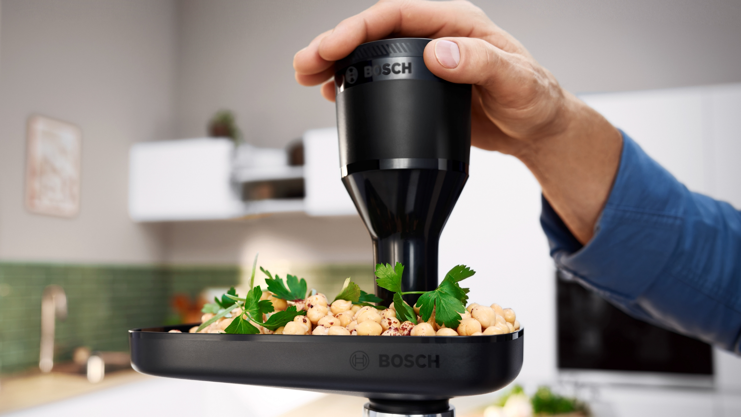 Hand hält Bosch-Aufsatz über Schüssel mit Kichererbsen und Petersilie.