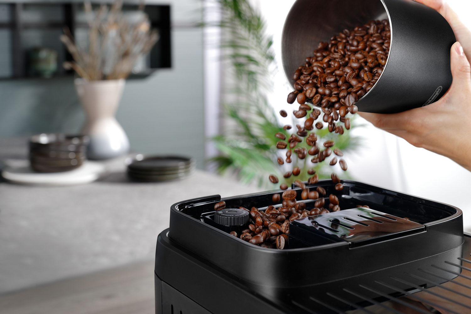 Granos de café marrones caen de un recipiente negro a una cafetera.