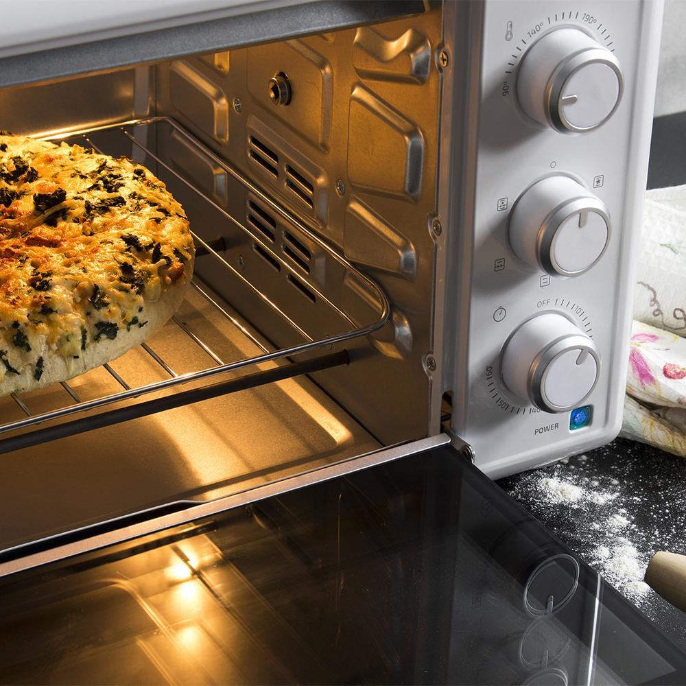 Una pizza redonda, dorada y con espinacas y queso se está horneando en un horno blanco.