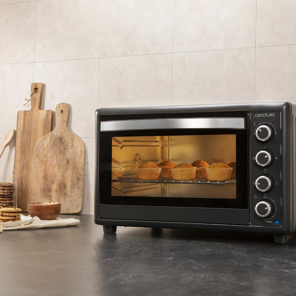 Un horno negro con muffins horneándose dentro está sobre una encimera. Tablas de cortar de madera están detrás.