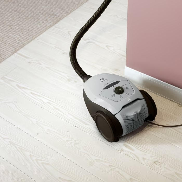 Un aspirateur blanc et gris avec un tuyau noir sur un parquet clair.