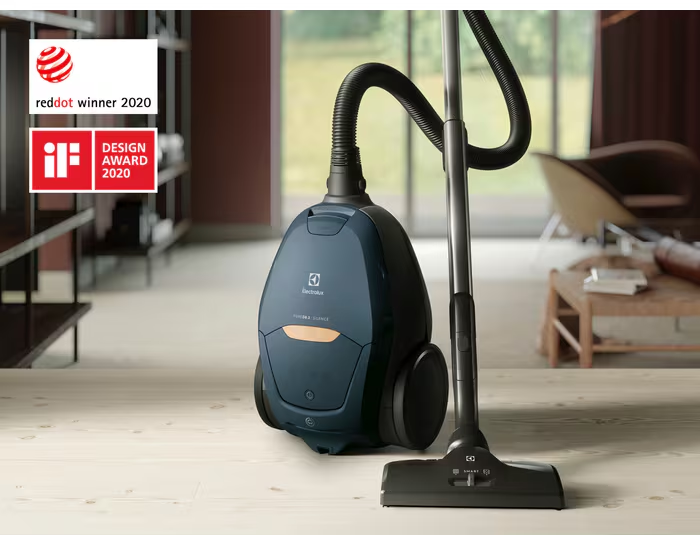 Un aspirateur bleu avec tuyau et manche se tient sur un plancher en bois.