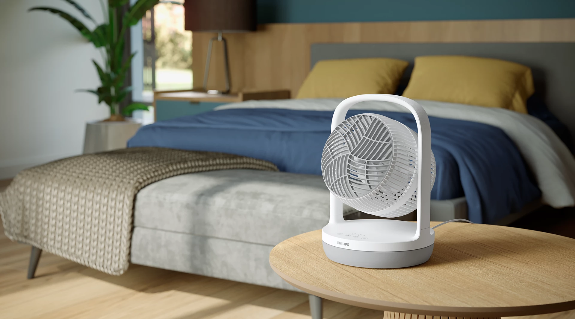 Ein weißer Ventilator steht auf einem Holztisch vor einem Bett mit blauer Decke.