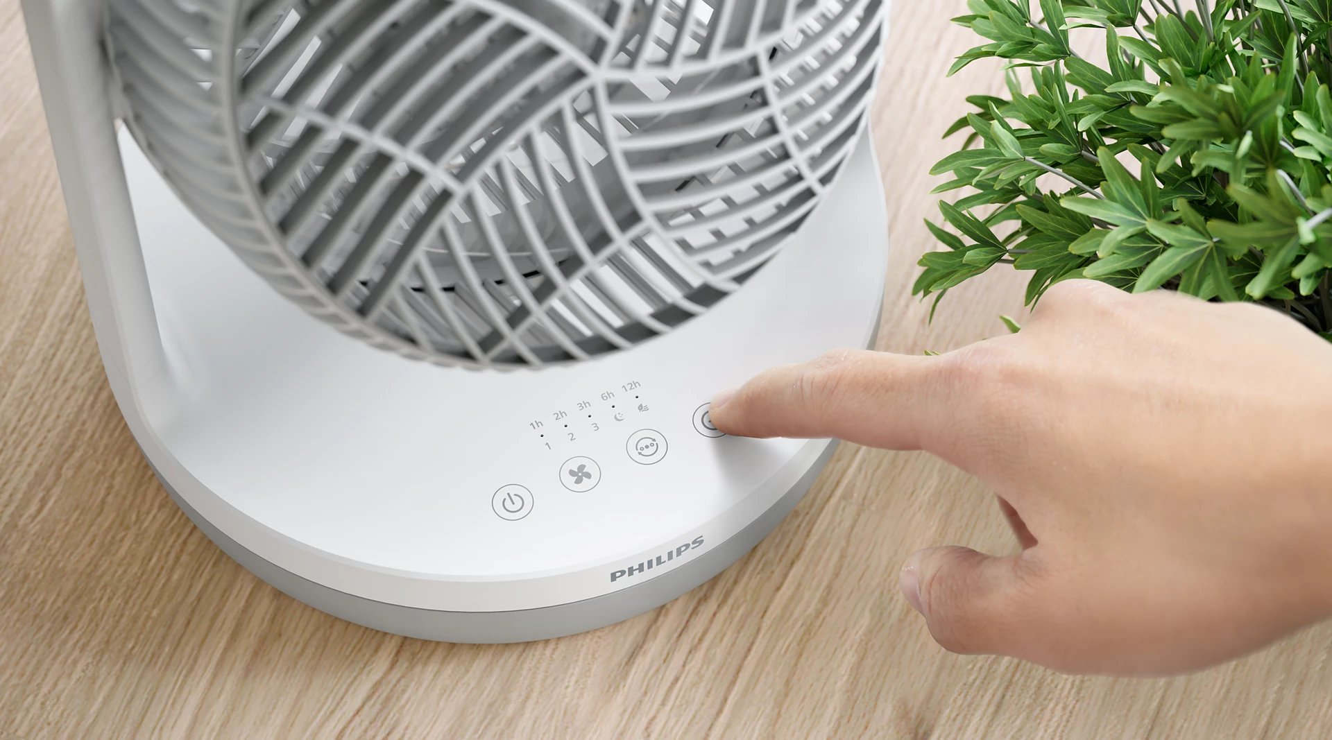 Eine Hand drückt einen Knopf auf einem weißen Ventilator mit Philips-Logo.
