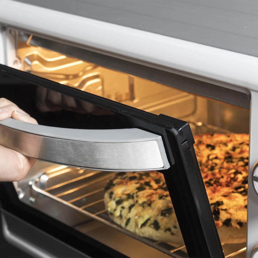 Una persona abre la puerta de un horno tostador con dos pizzas horneándose.