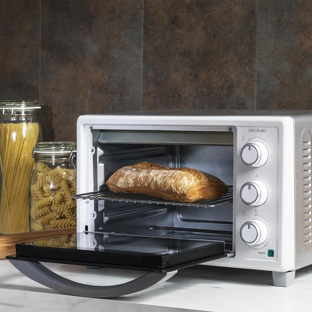 Una hogaza de pan se está horneando en un horno pequeño. Dos tarros de pasta a la izquierda.
