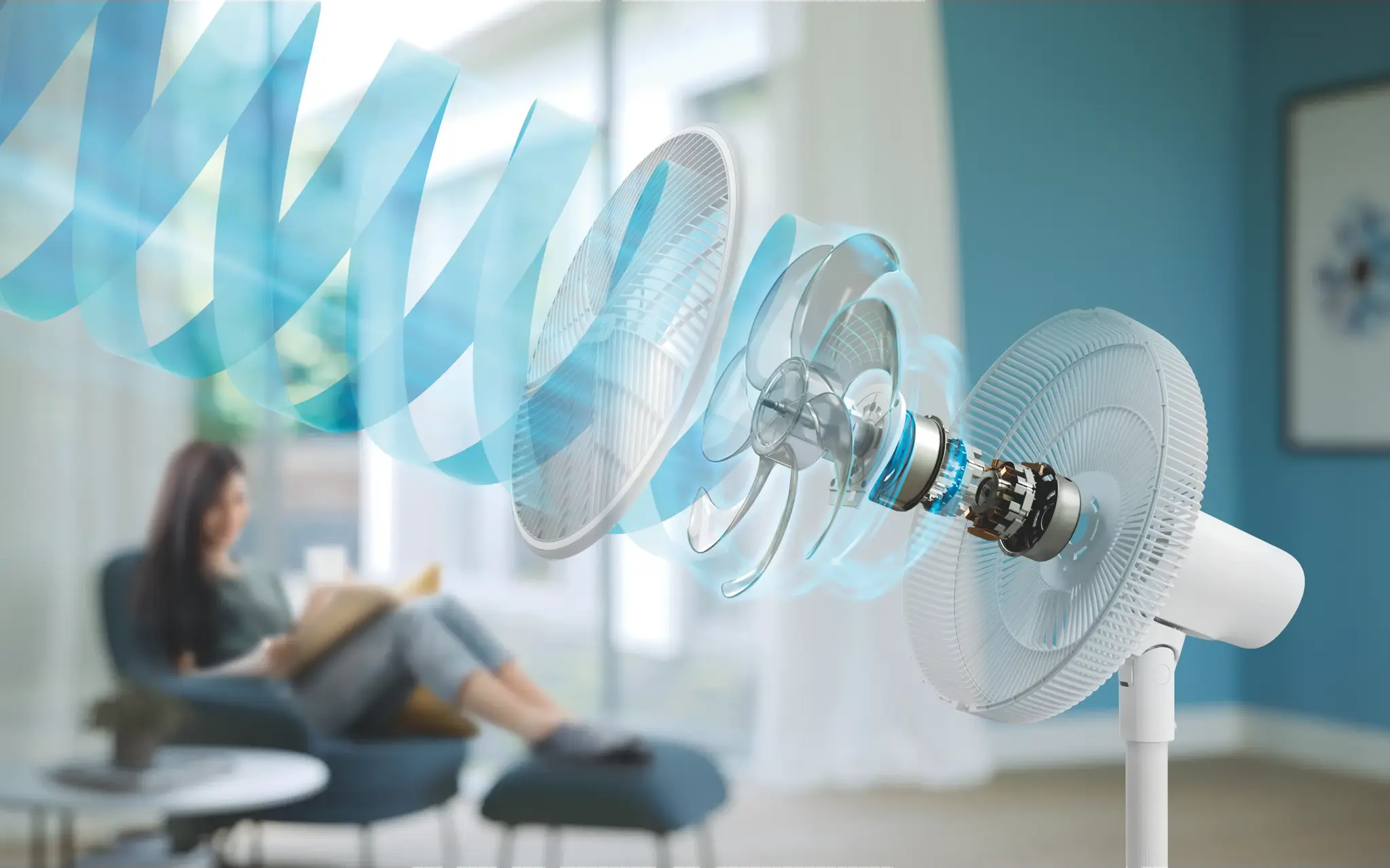 Ein weißer Ventilator mit Rotorblättern und Luftstrom. Eine Frau sitzt im Hintergrund.