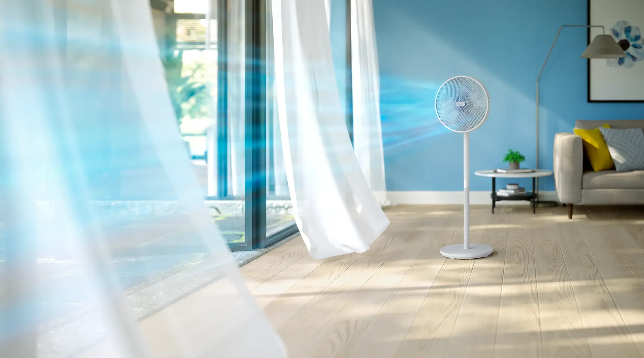 Ein Ventilator bläst Luft in ein Wohnzimmer mit weißen Vorhängen.
