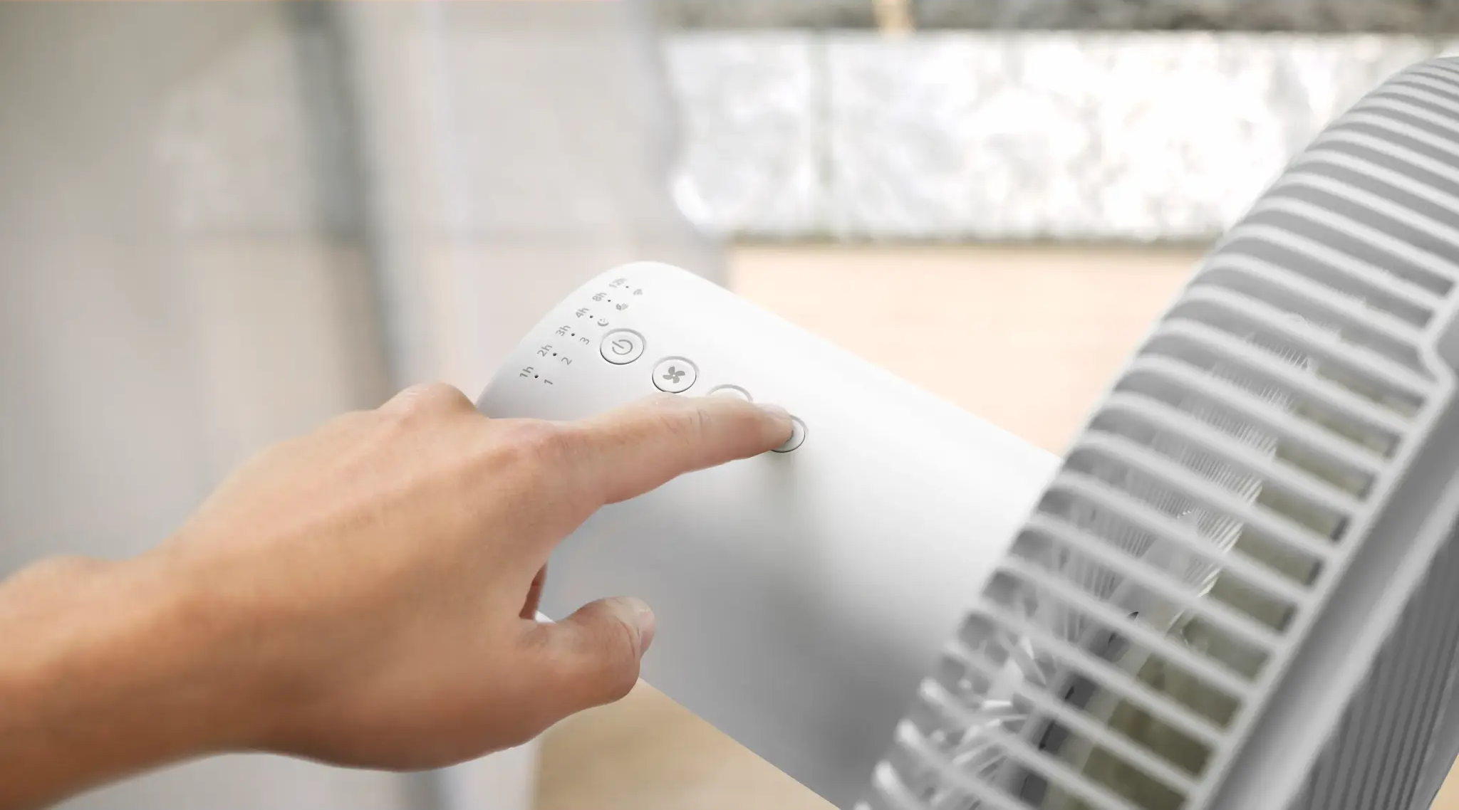 Eine Hand drückt einen Knopf an einem weißen Ventilator.