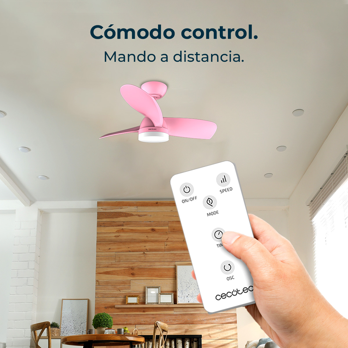 Una mano sostiene un mando a distancia blanco para un ventilador de techo rosa.