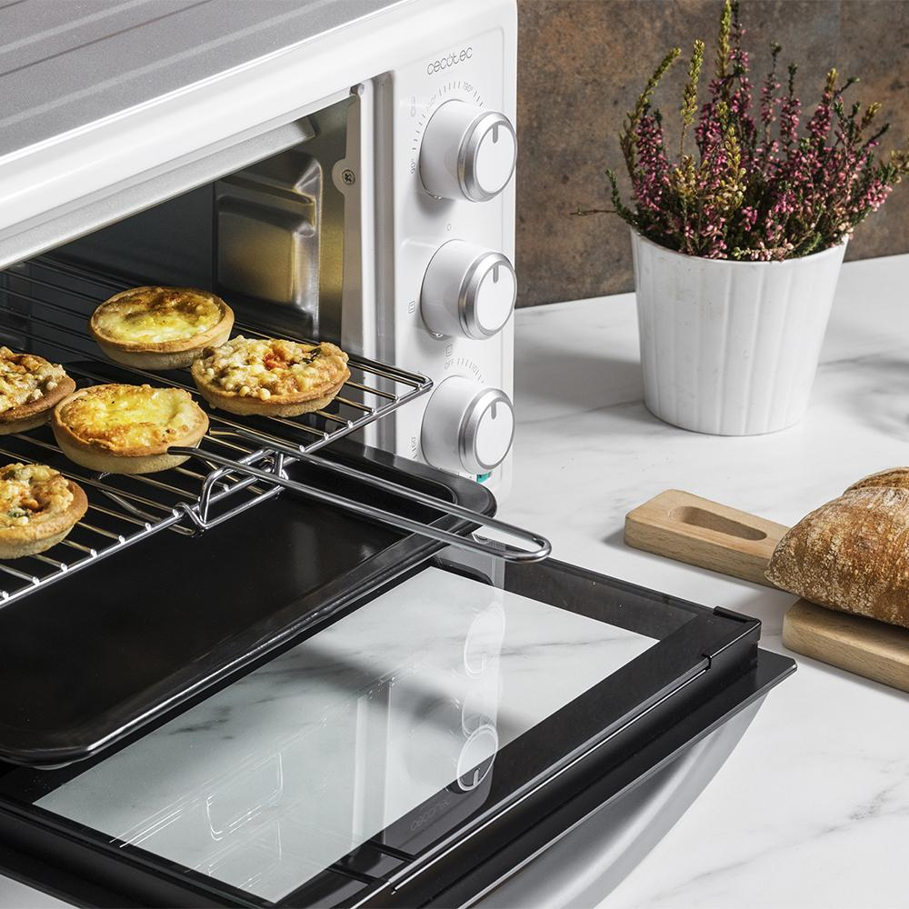 Mini horno con tartaletas en rejilla, pan y planta en maceta.