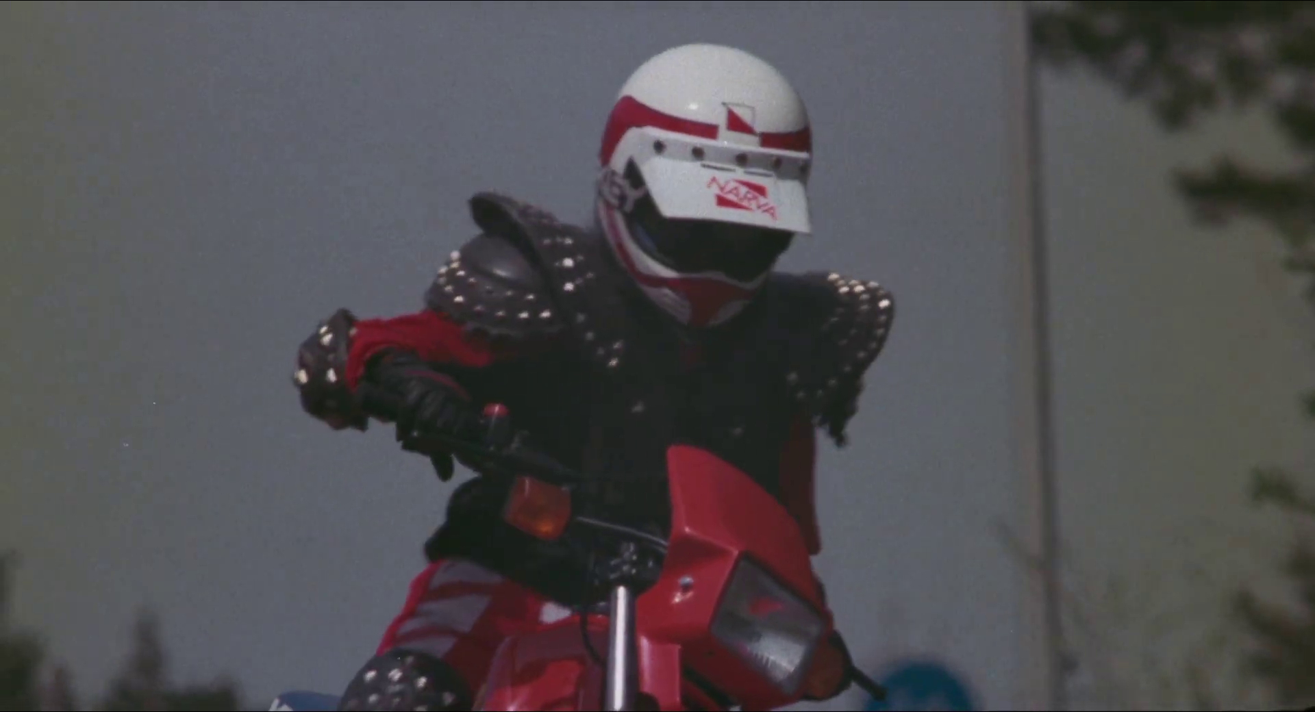 Eine Person in einem weiß-roten Helm und schwarzer Rüstung fährt ein rotes Motorrad.