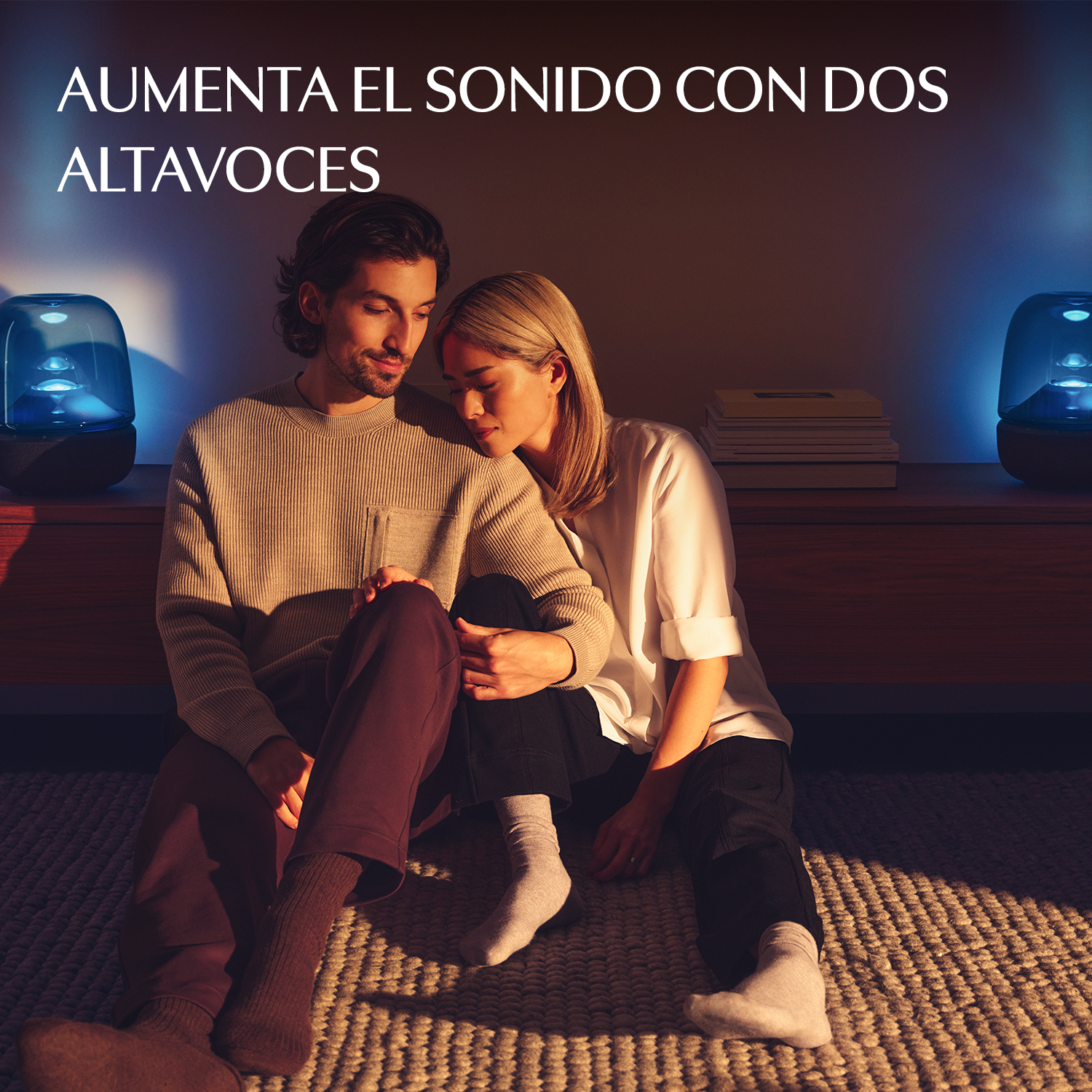 Una pareja se sienta en una alfombra frente a dos altavoces azules.
