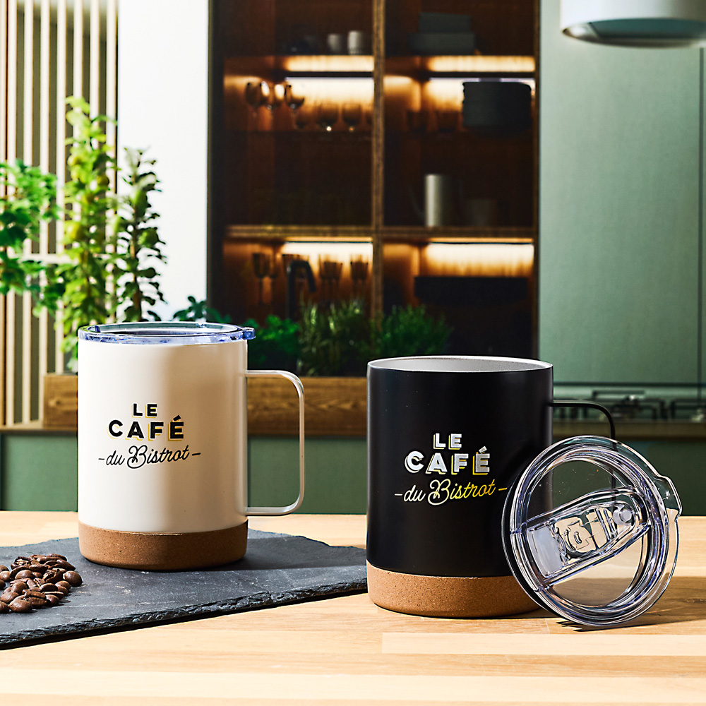 Dos tazas térmicas, blanca y negra, sobre una mesa de madera con granos de café.