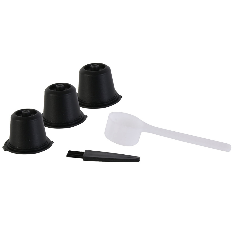 Tres cápsulas de café negras, una cuchara blanca y un cepillo pequeño sobre fondo blanco.