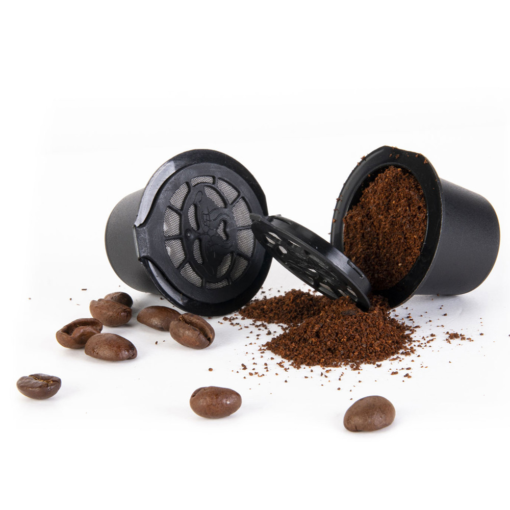 Dos cápsulas de café abiertas con café molido y granos de café sobre fondo blanco.