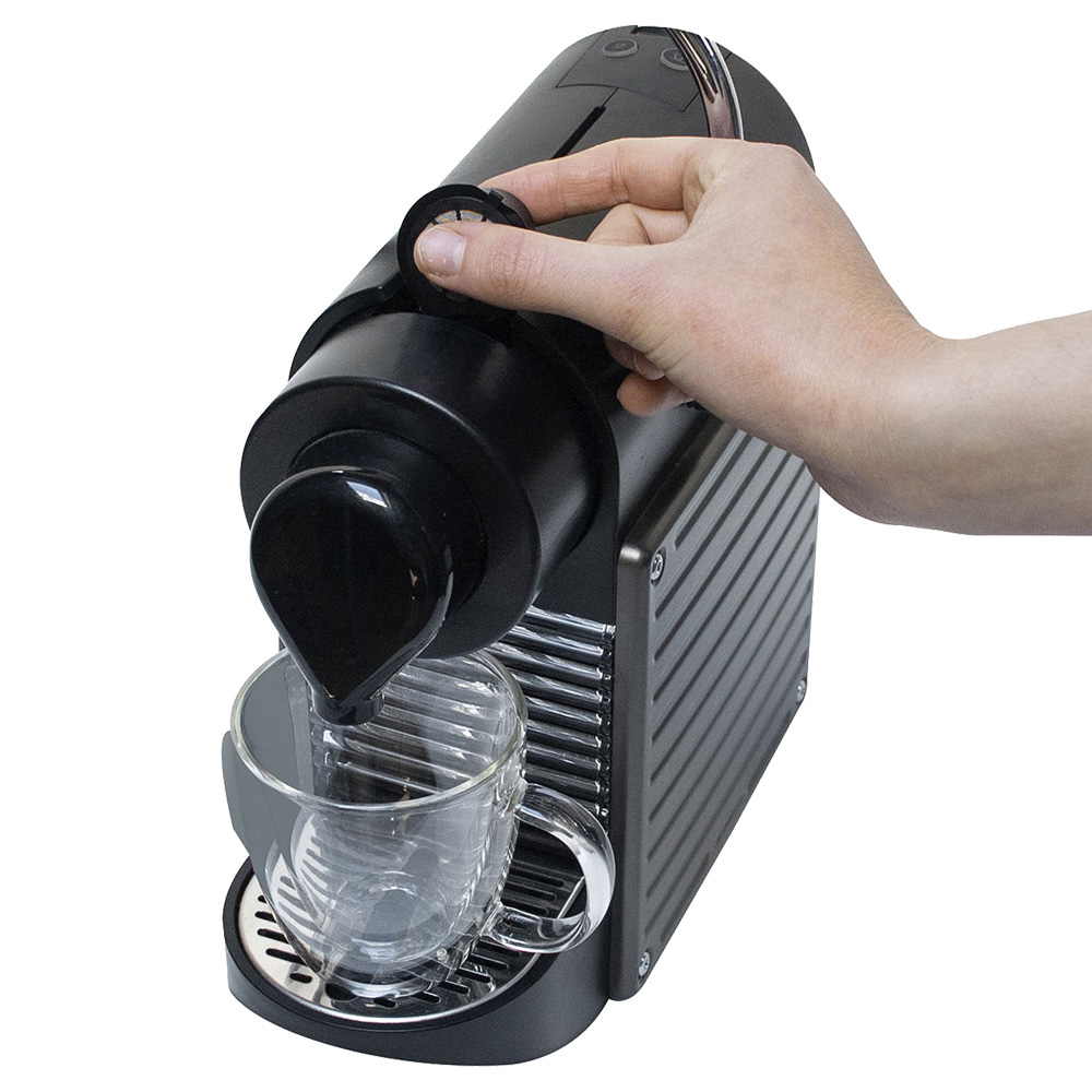 Una mano inserta una cápsula de café en una cafetera mientras el café fluye hacia una taza.