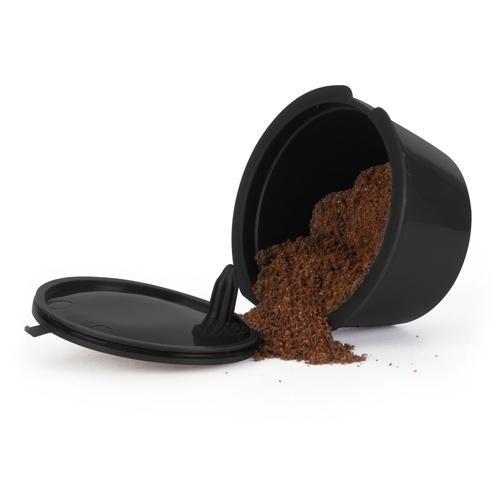 Una cápsula de café negra con posos de café sueltos derramándose.