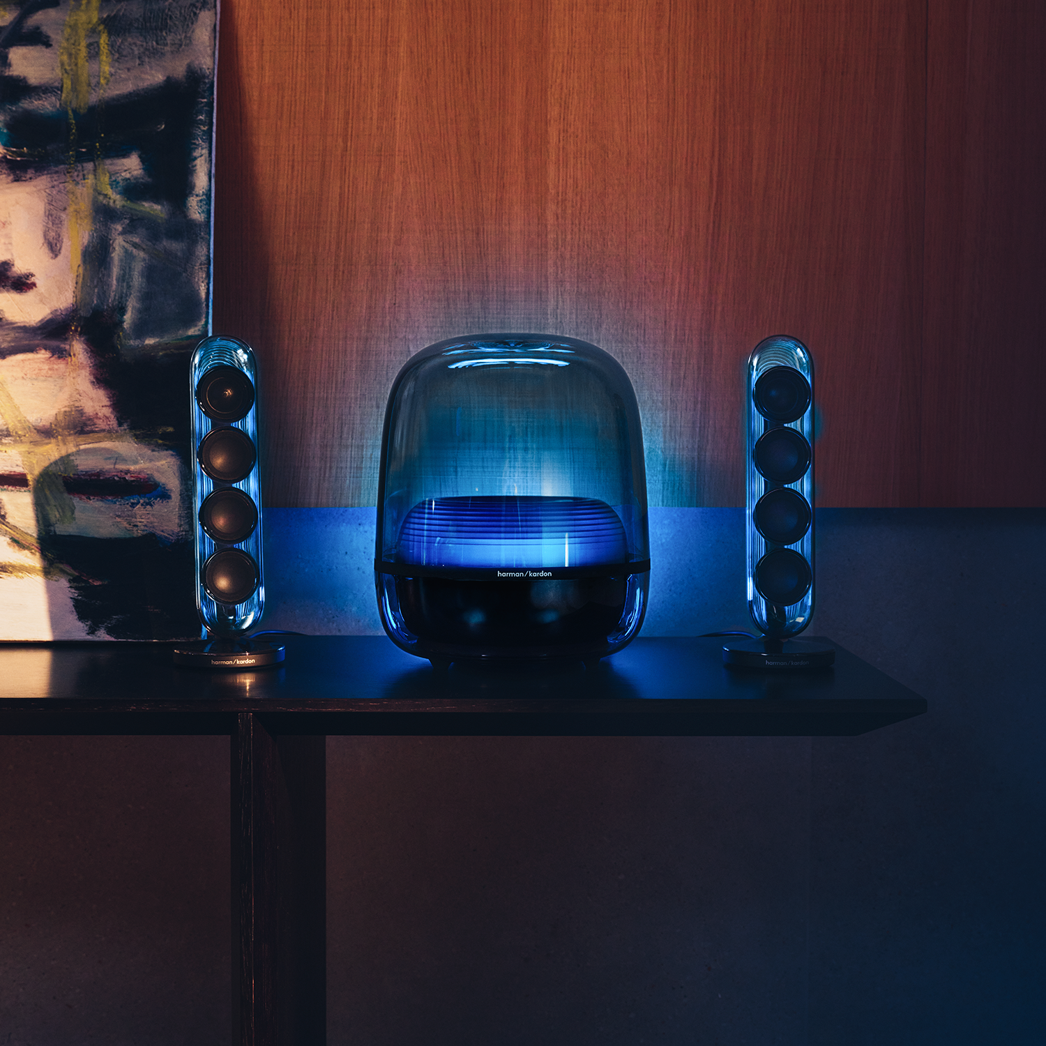 Dos altavoces delgados flanquean un altavoz transparente más grande con iluminación azul.