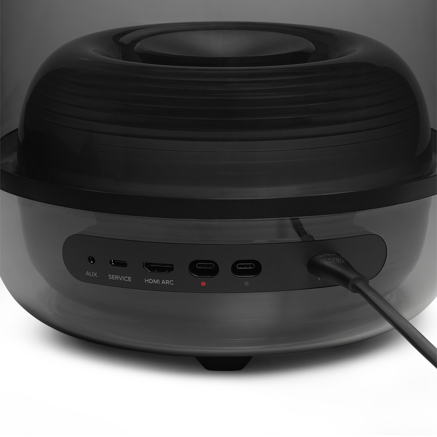 Panel trasero de altavoz negro con puertos AUX, SERVICE, HDMI ARC y USB-C. Un cable está enchufado.