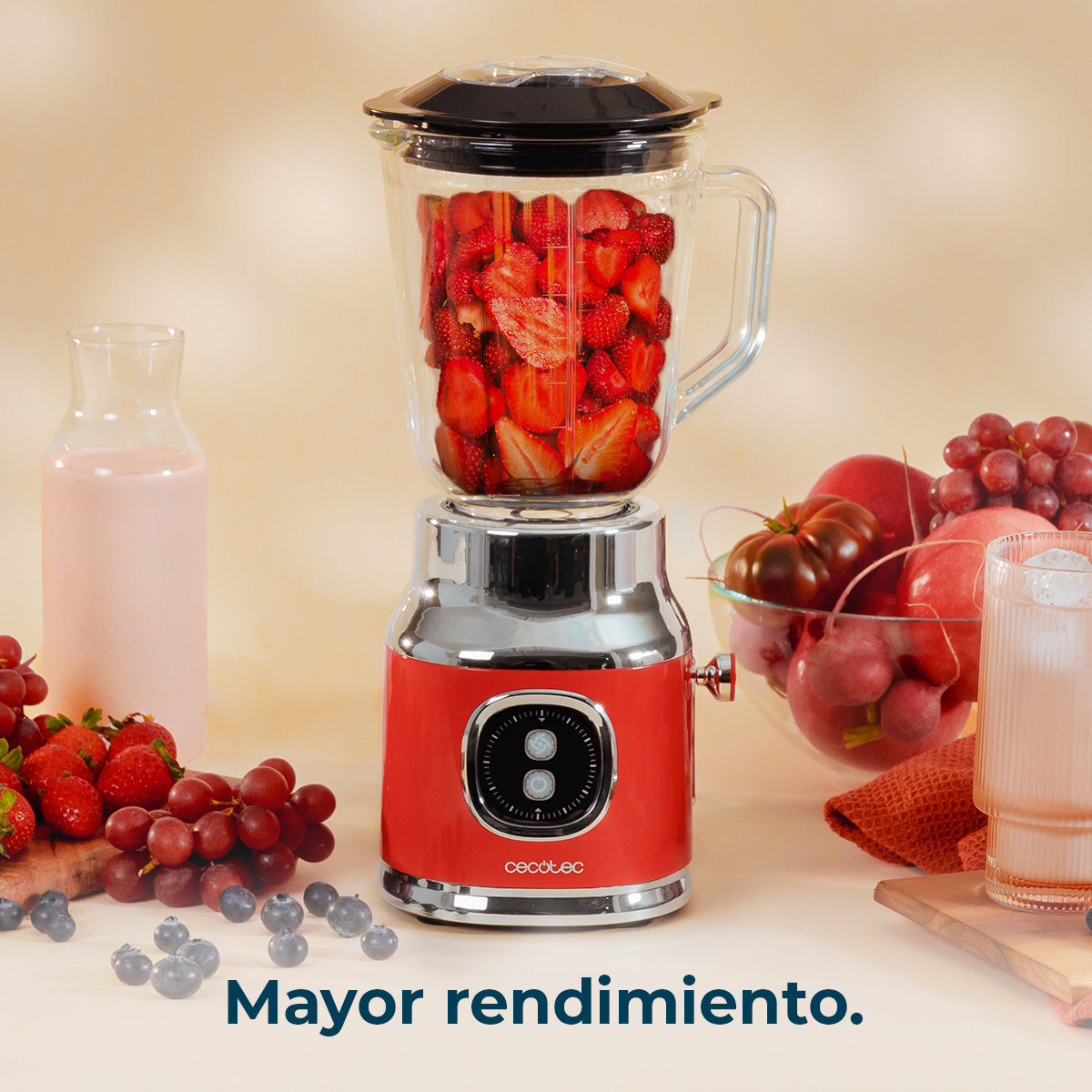Una licuadora roja llena de fresas, con frutas y una bebida al lado.