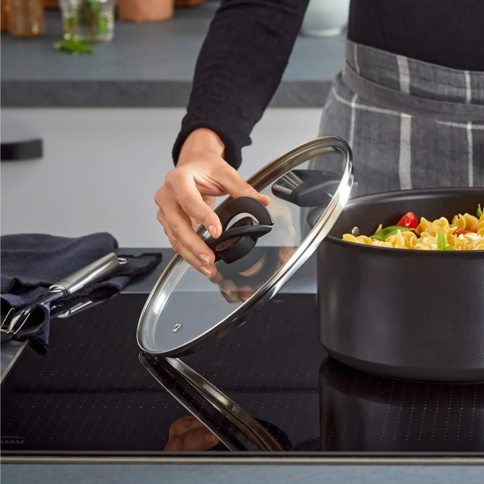 Ręka podnosi szklaną pokrywkę z garnka z makaronem na płycie indukcyjnej.