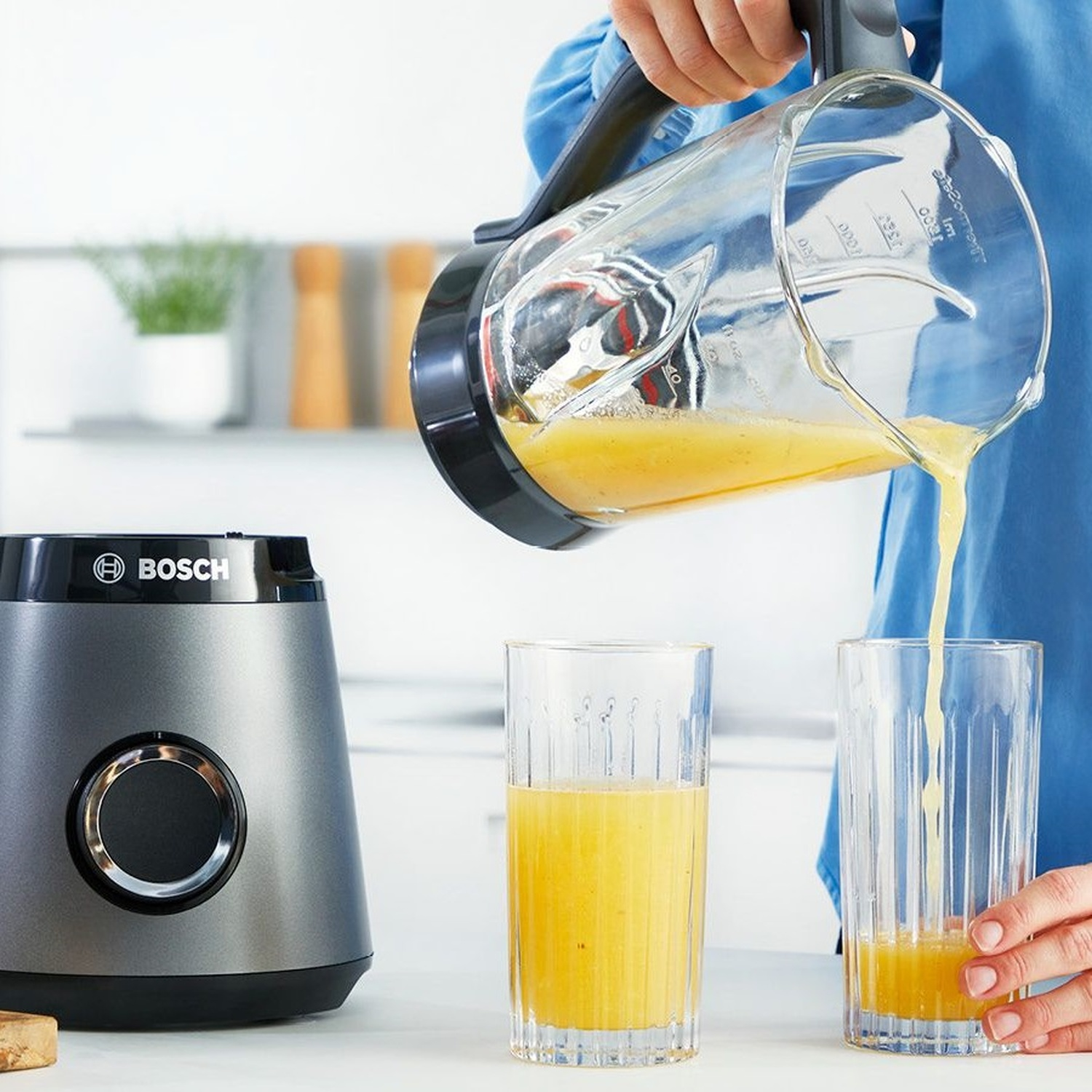 A grey blender sits on a countertop as juice is poured into two glasses.
